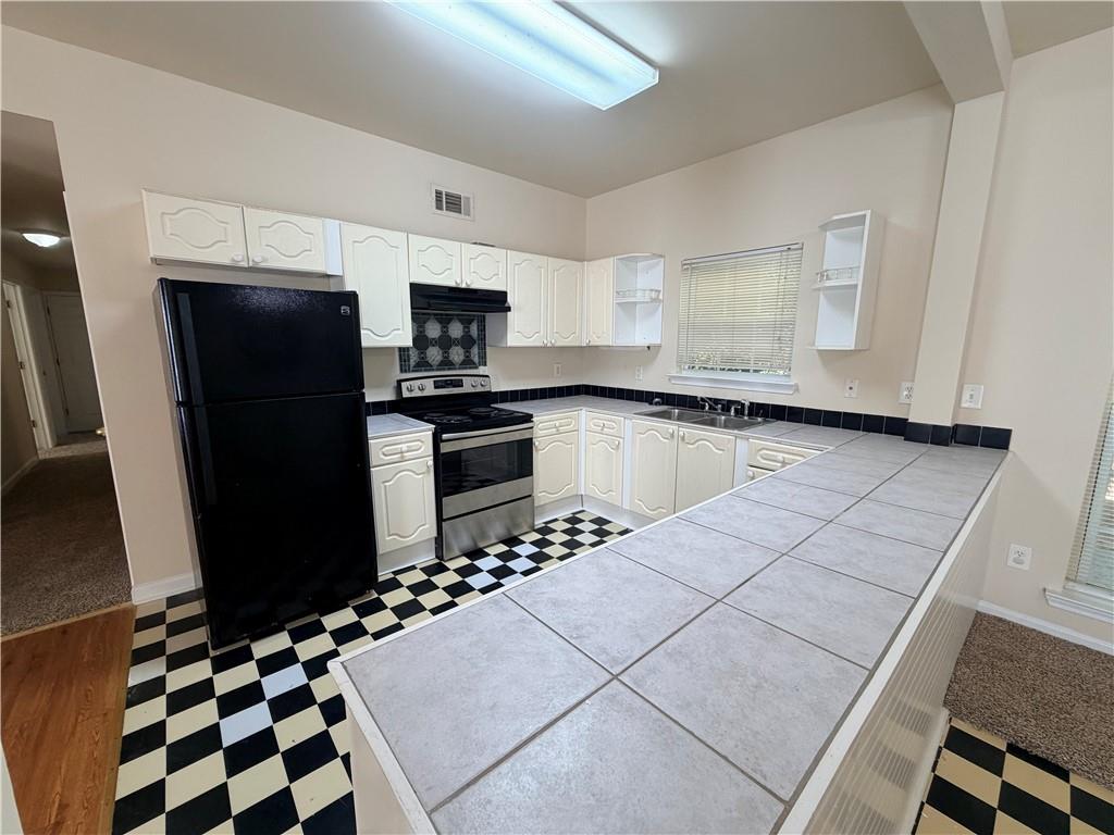 Kitchen with white cabinets, black appliances, checkerboard flooring, and a large tiled peninsula.
