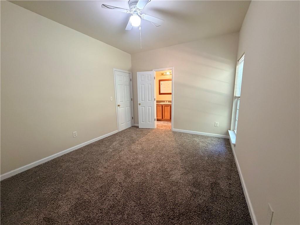 Empty carpeted bedroom with a ceiling fan and an open doorway to the bathroom.