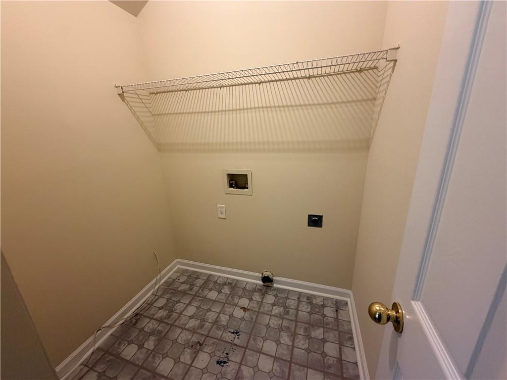 Empty laundry room with washer and dryer hookups and a long wire shelf.