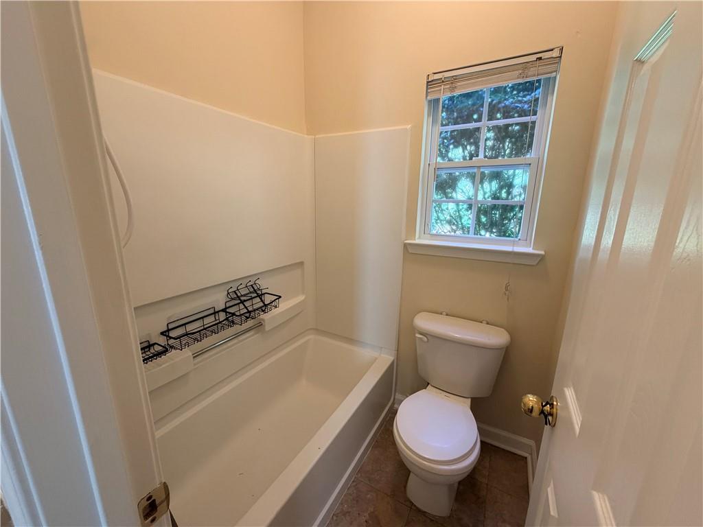 Bathroom with a white bathtub, built-in wire rack, toilet, and a window overlooking trees.