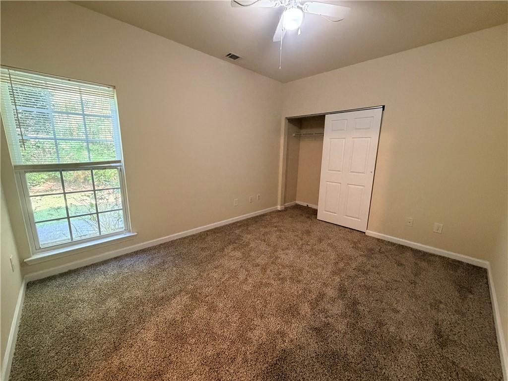 Empty bedroom with brown carpet, a large window, and an open closet.