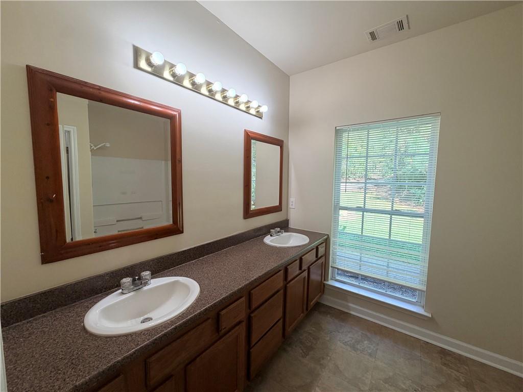Bathroom with a double-sink vanity, wood cabinets, and a large window with blinds.