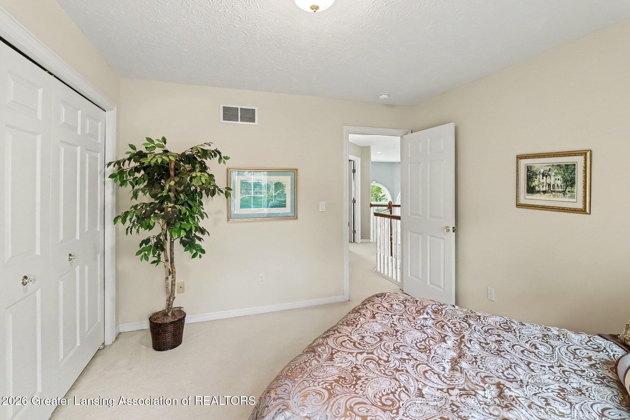 Bedroom with white sliding closet doors, a patterned bed, and a potted indoor tree.