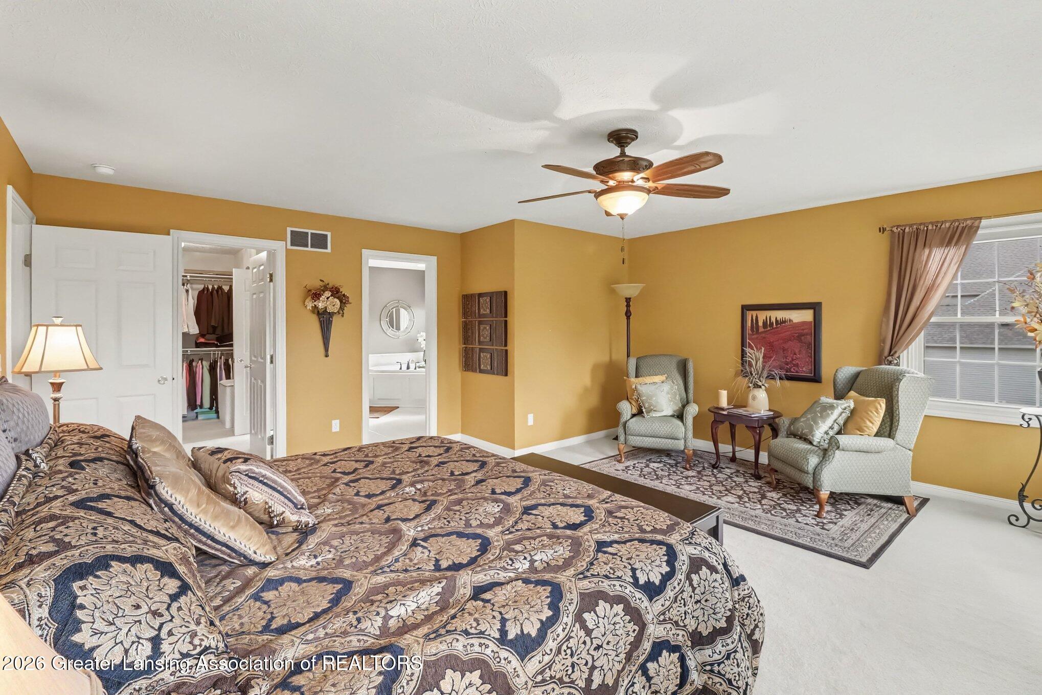Bedroom with a large patterned bed, mustard-yellow walls, and a seating area by the window.