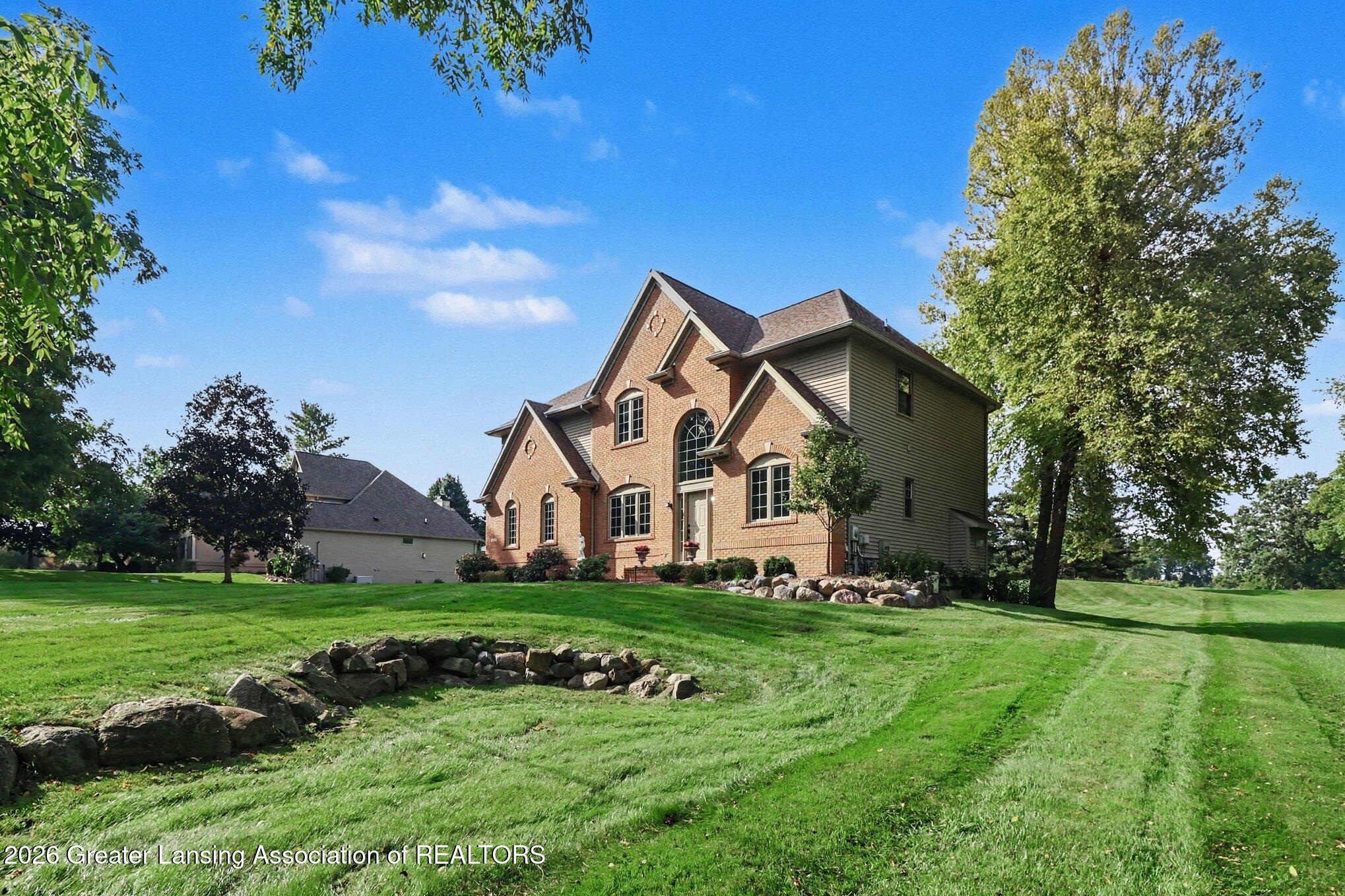 Two-story brick house with arched windows, mature trees, and a broad lawn.