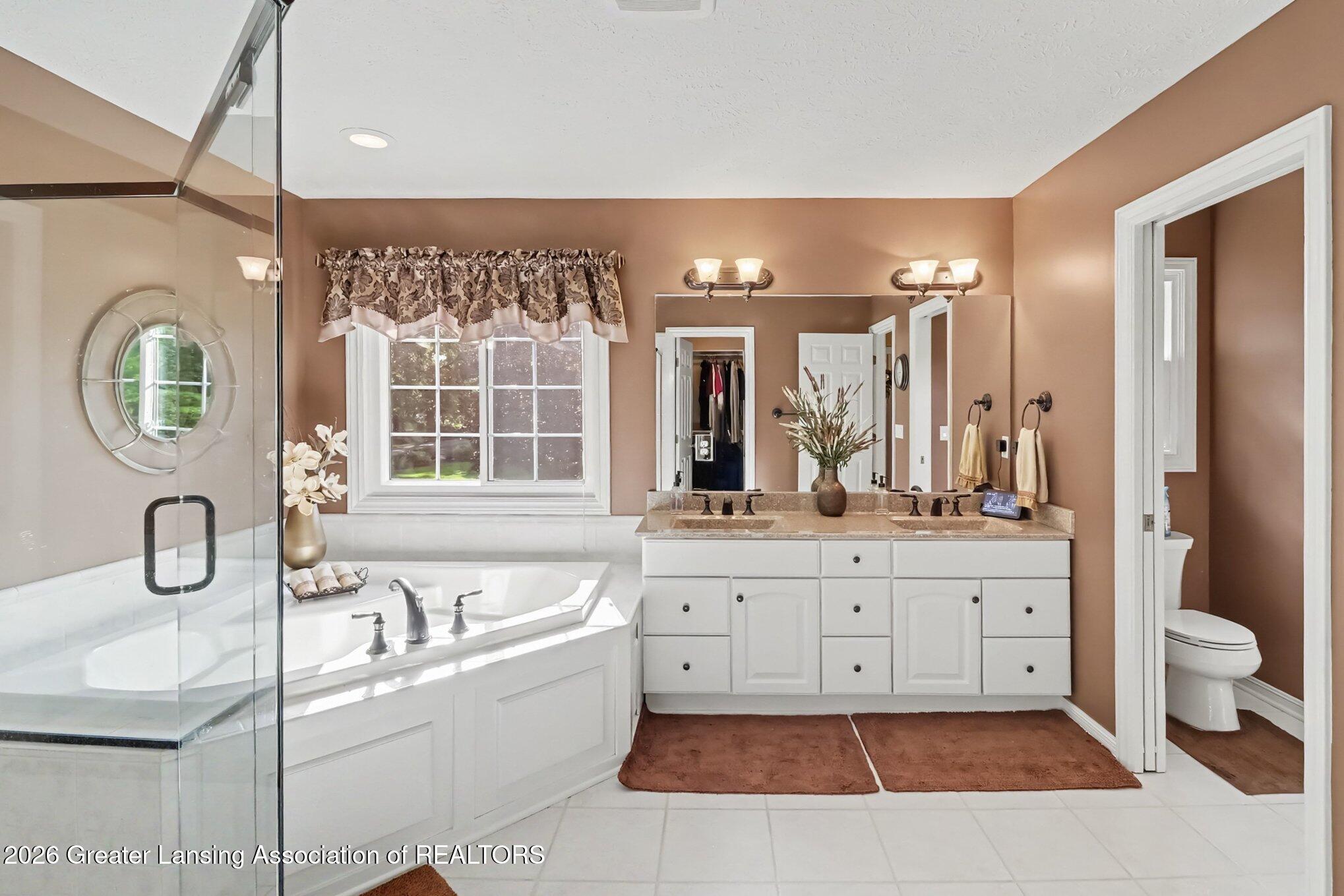 Spacious bathroom with a jetted corner tub, glass shower, window, and double-sink vanity.