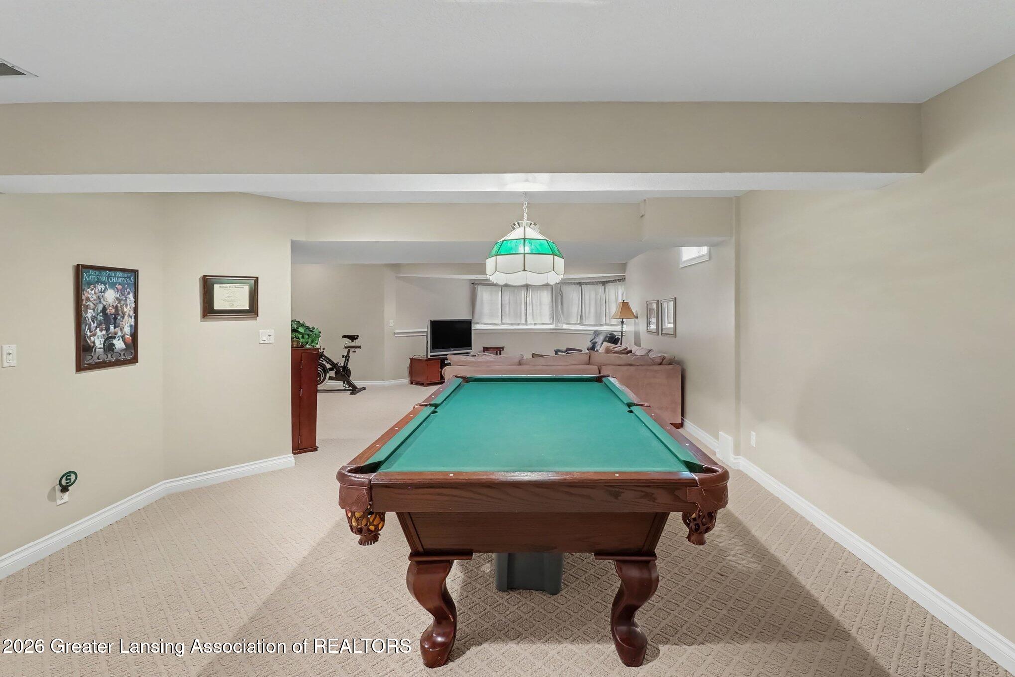 Furnished recreation room with a green-felt pool table and a seating area in the background.