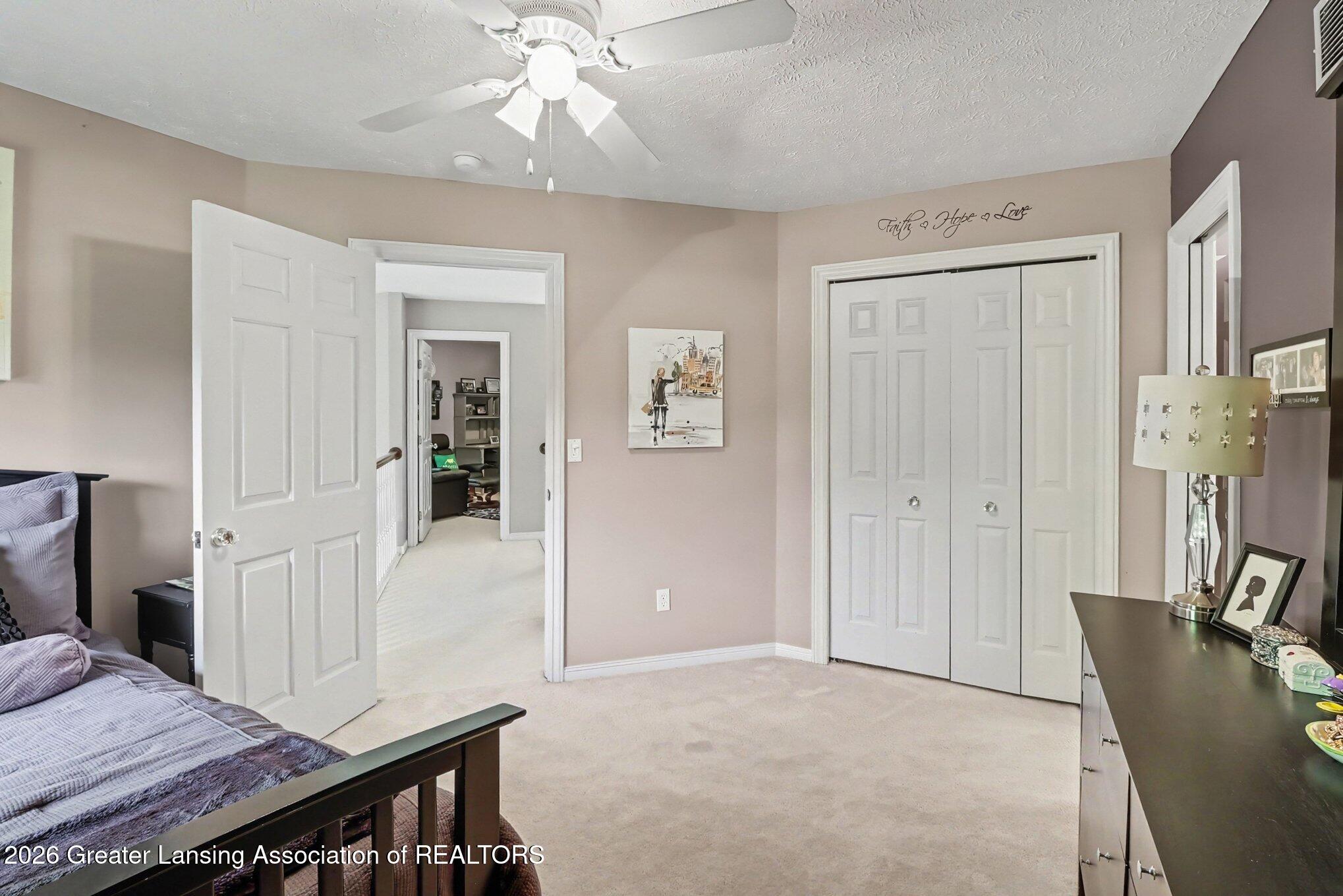 Bedroom with beige walls, white double closet doors, ceiling fan, and doorway to an adjoining room.