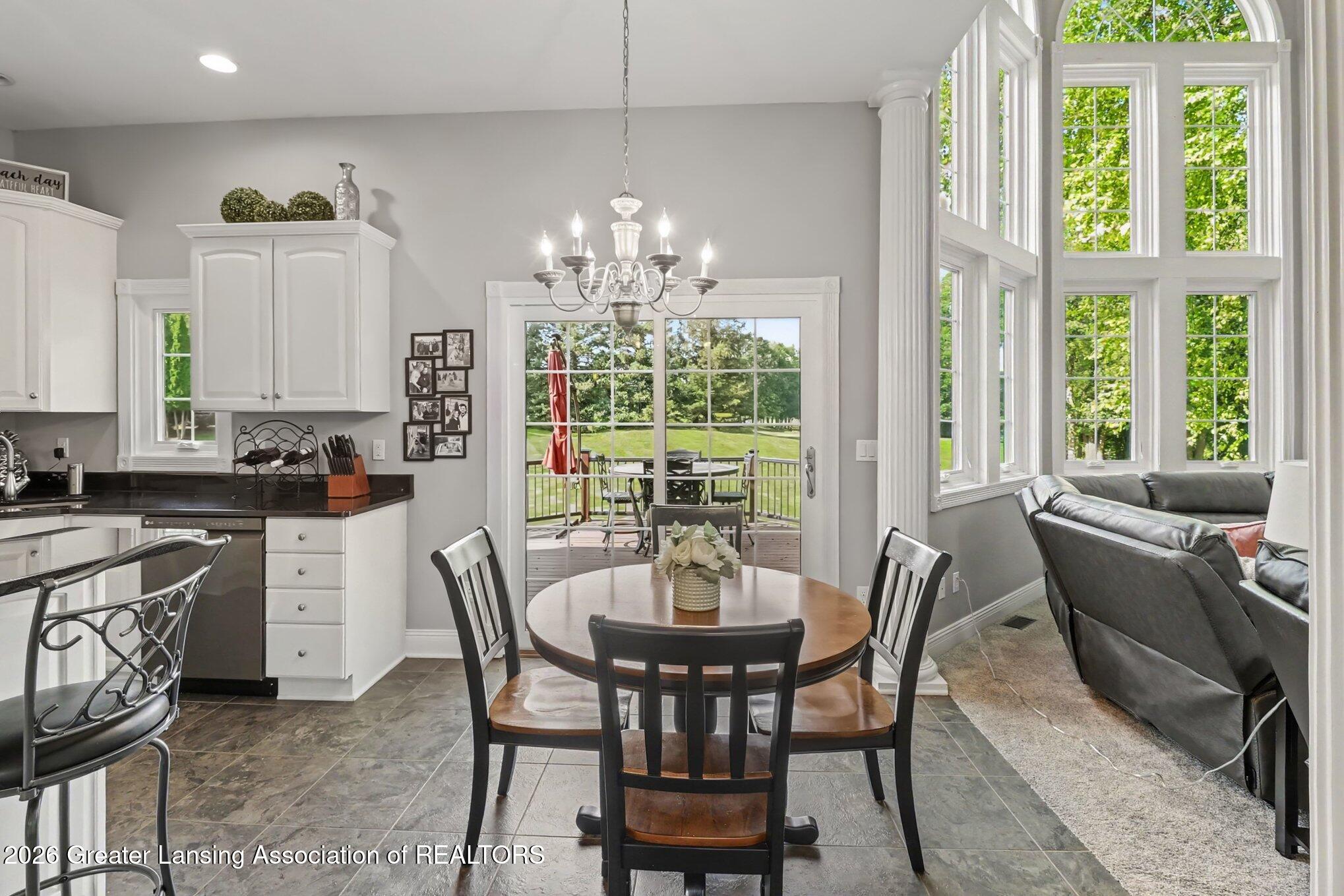 Open kitchen and dining area with a round wooden table, chandelier, deck doors, and tall arched windows.