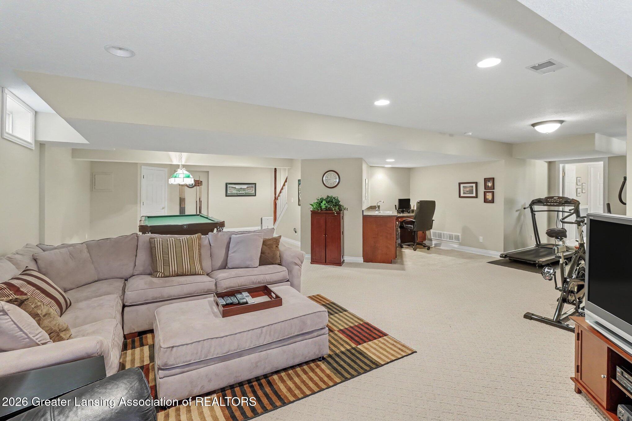 Furnished basement recreation room with a pool table, sectional sofa, desk, treadmill, and exercise bike.