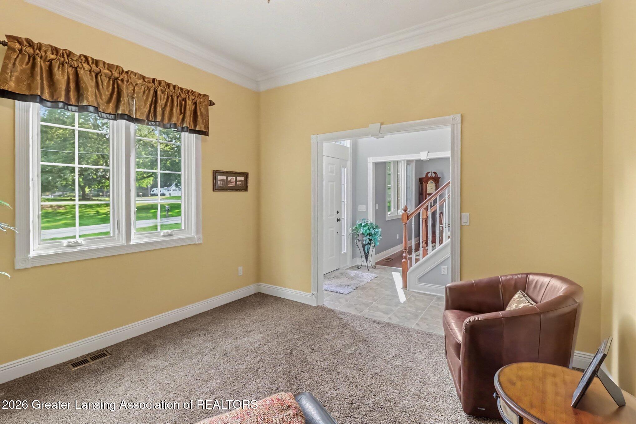 Sitting room with yellow walls, carpet, two windows, and a leather chair by the entry hall.