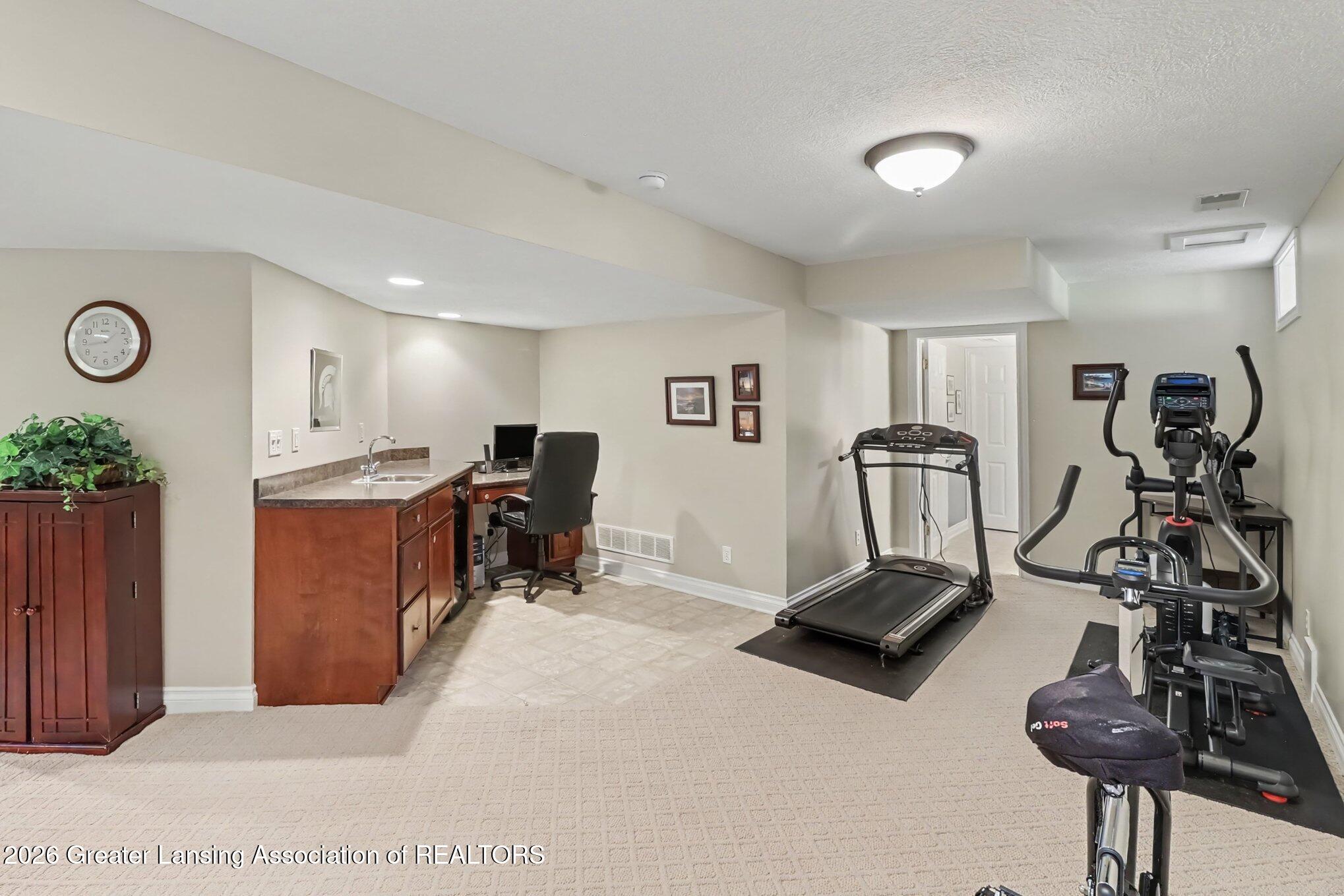 Basement home gym with a treadmill, elliptical, and built-in desk with sink.