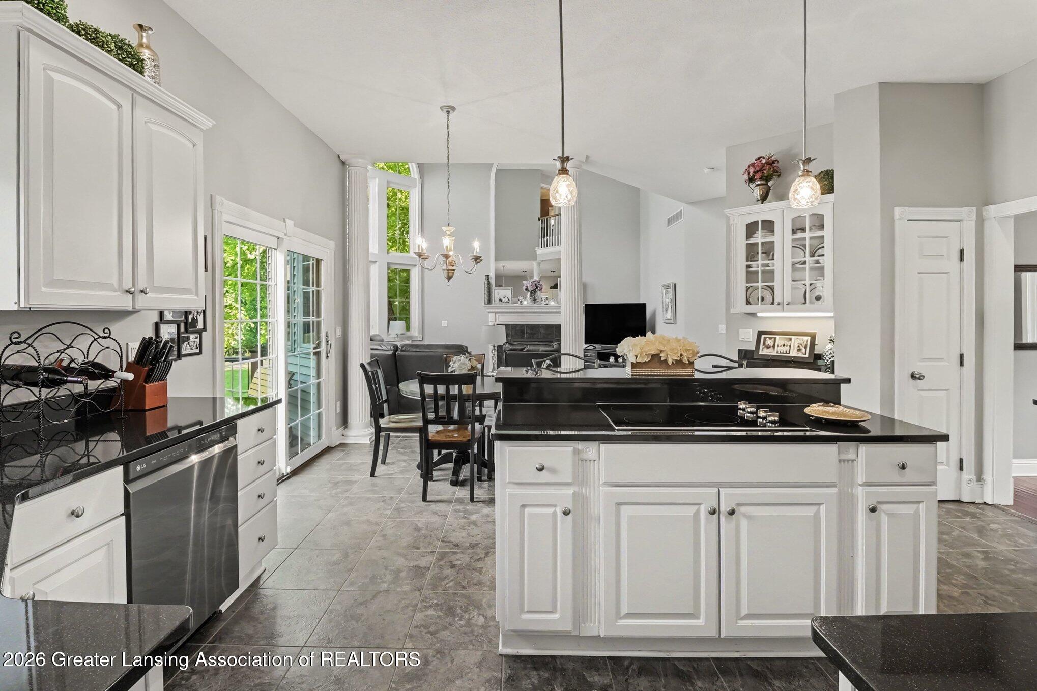 Open-plan kitchen with white cabinets, black island cooktop, and glass doors opening toward the yard.