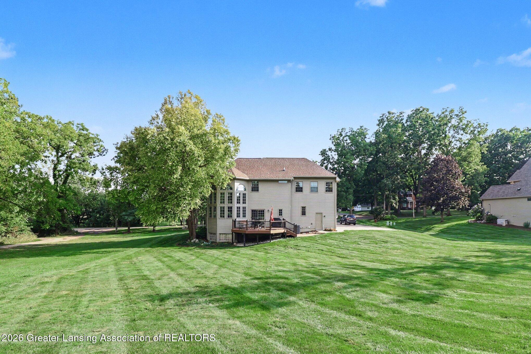 Home’s rear exterior with a raised deck, expansive lawn, and mature trees.