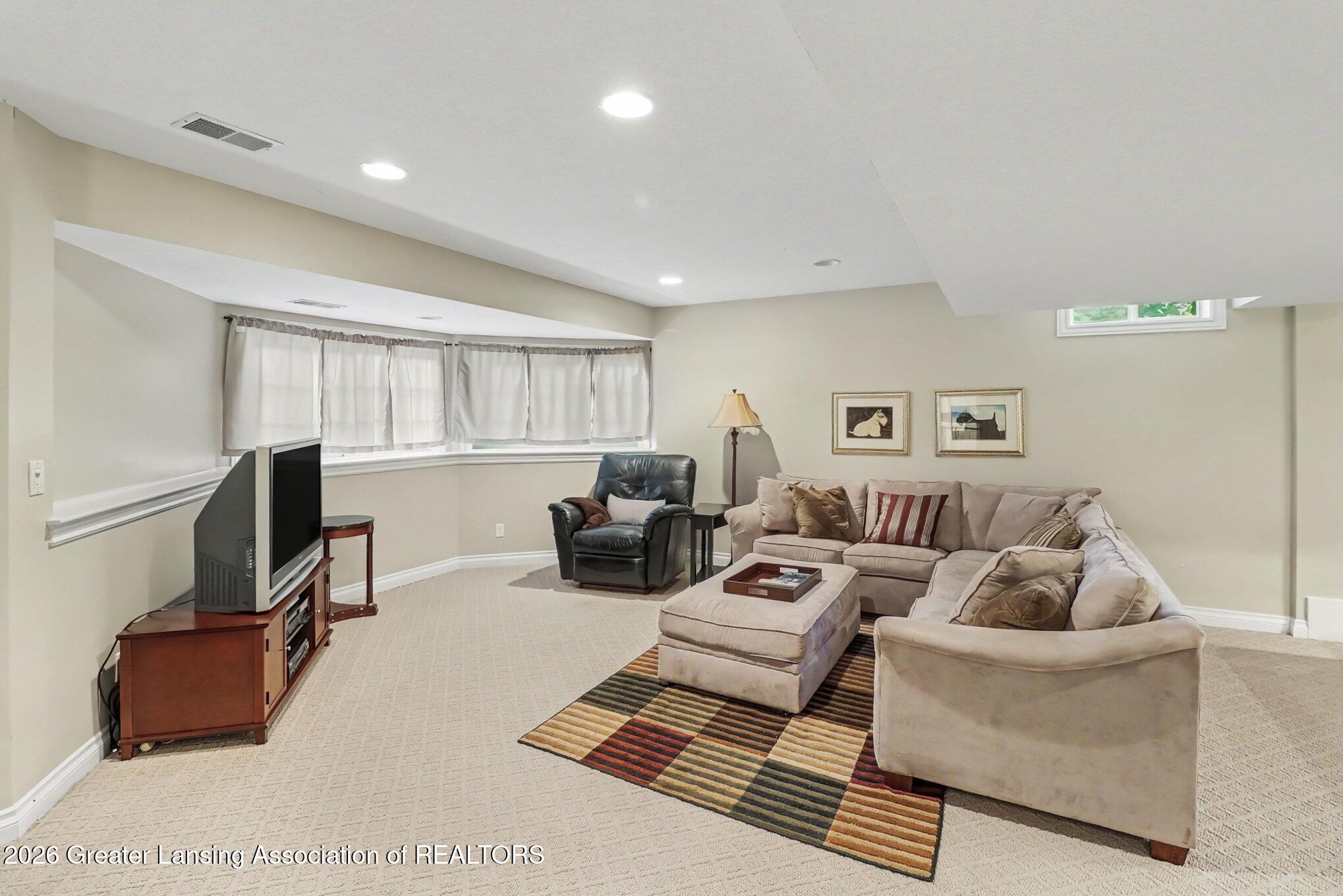 Furnished living room with a beige sectional, leather recliner, and colorful striped rug.