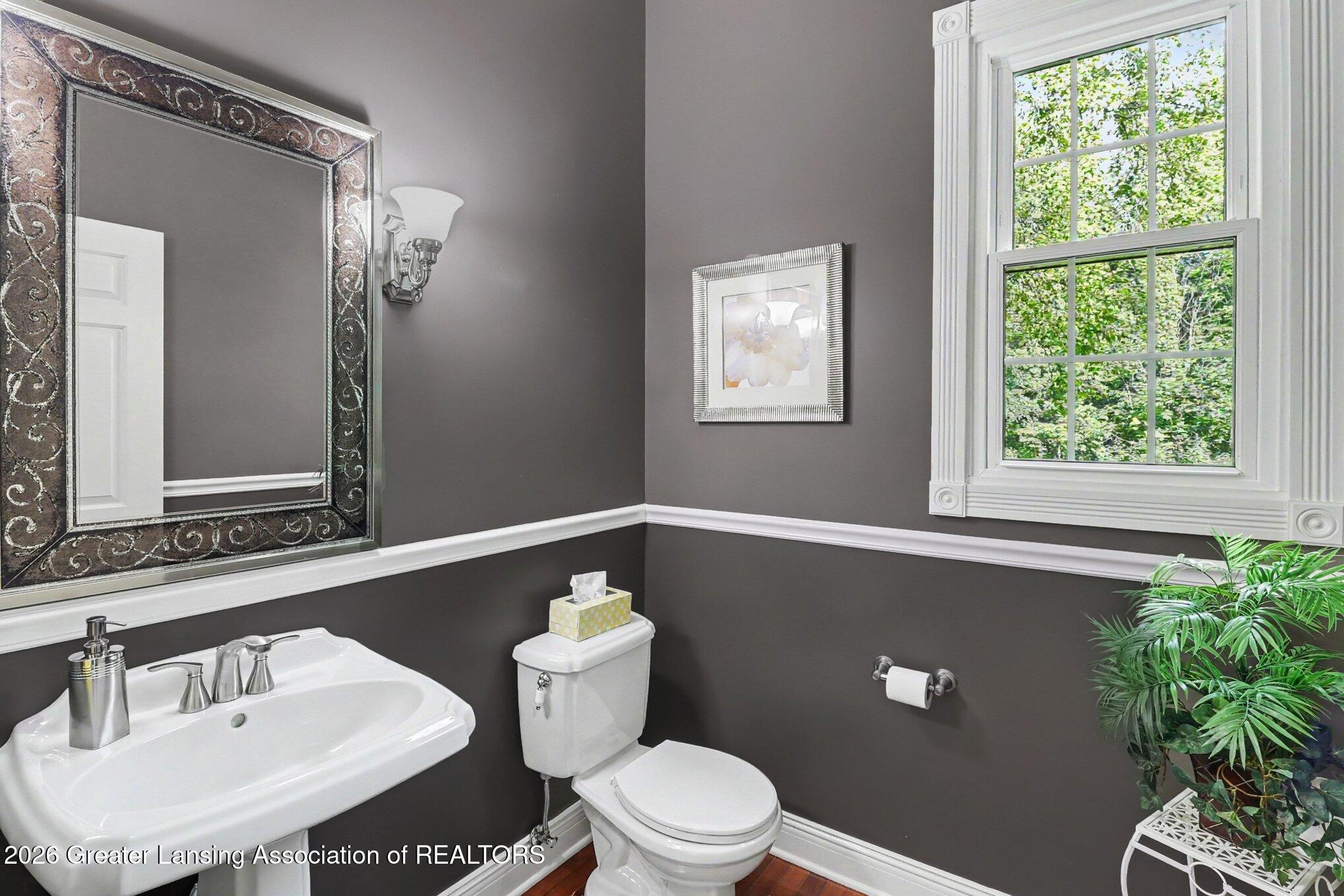 Bathroom with dark gray walls, ornate mirror, white pedestal sink, and a large window.
