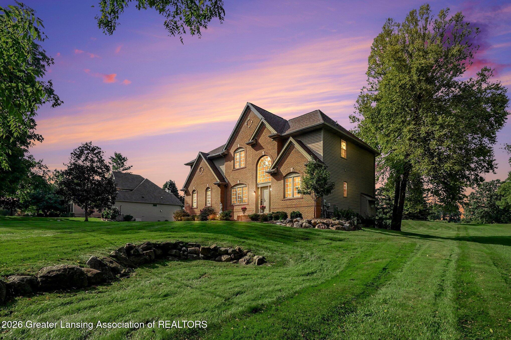 Brick home with illuminated arched windows and a broad lawn beneath a colorful dusk sky.