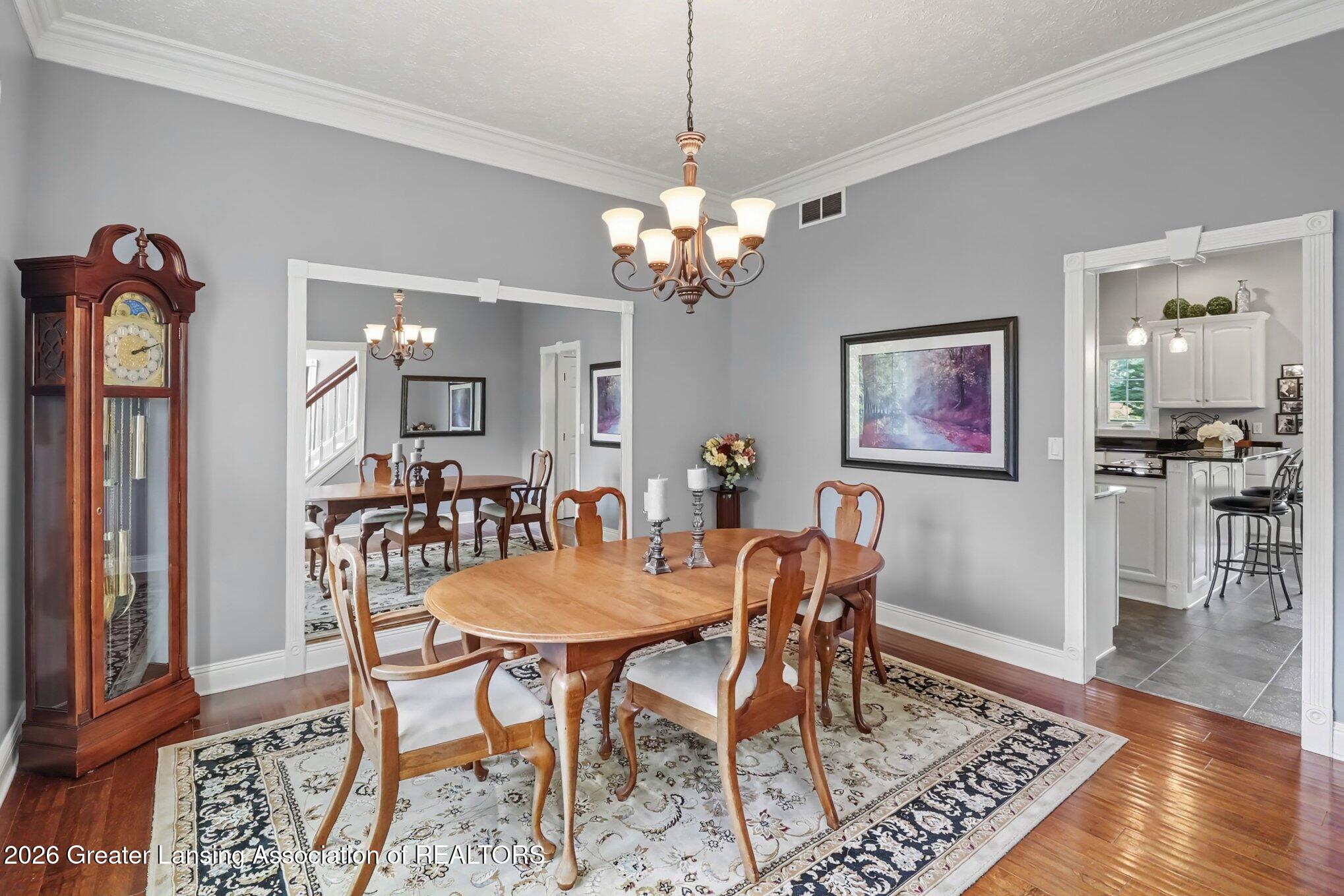 Furnished dining room with an oval wooden table, patterned rug, grandfather clock, and chandelier.