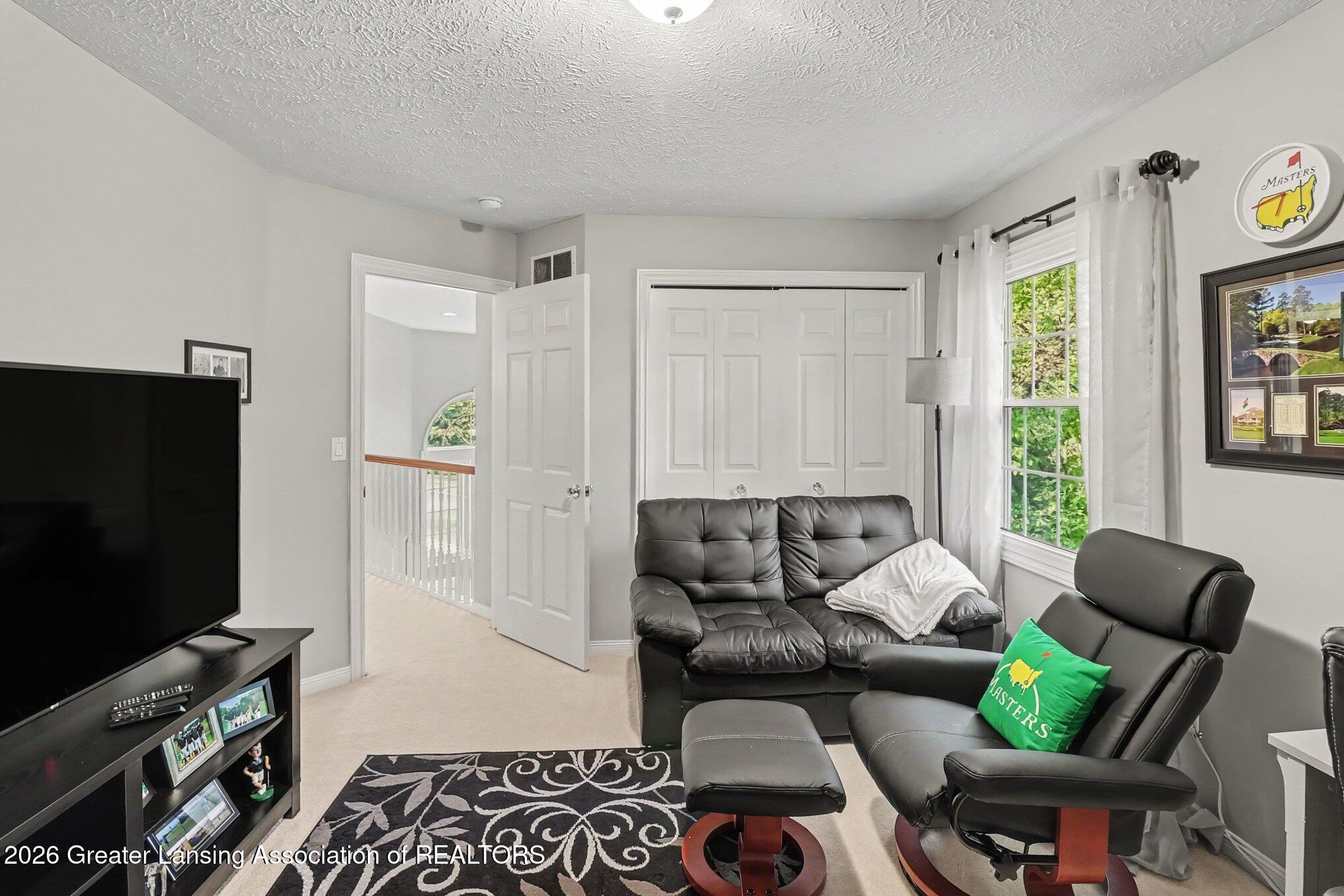 Furnished living room with black leather seating, a large television, and white closet doors.