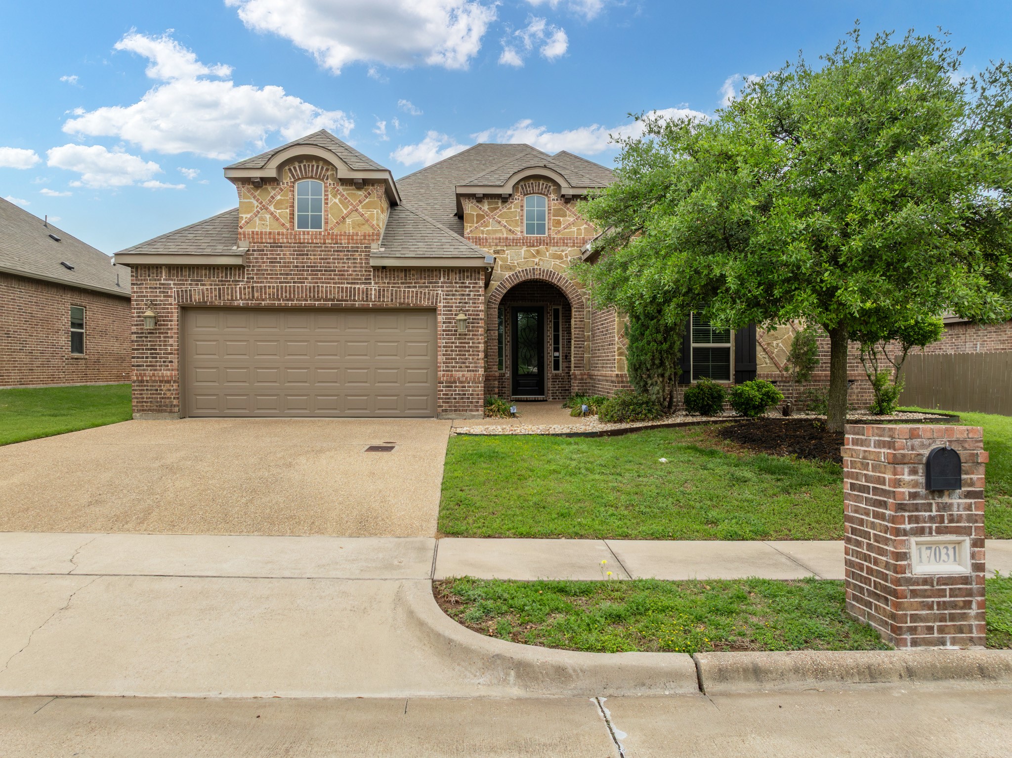 Two-story brick and stone house with a two-car garage, arched entry, and brick mailbox.