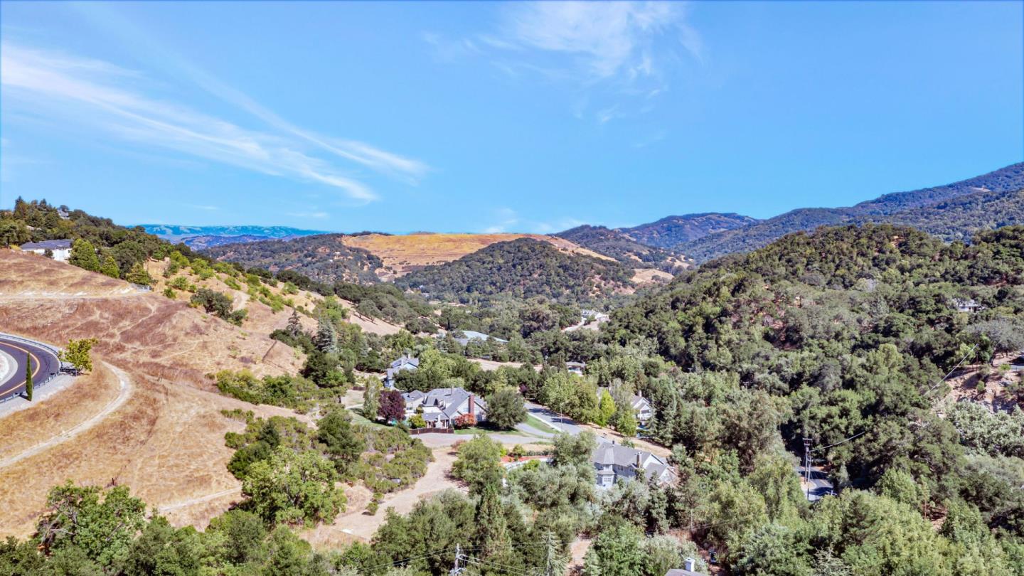 Aerial view of homes among wooded hills, dry golden slopes, and a winding road.
