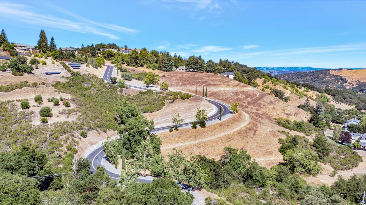 Aerial view of a winding road through dry rolling hills with scattered homes and trees.