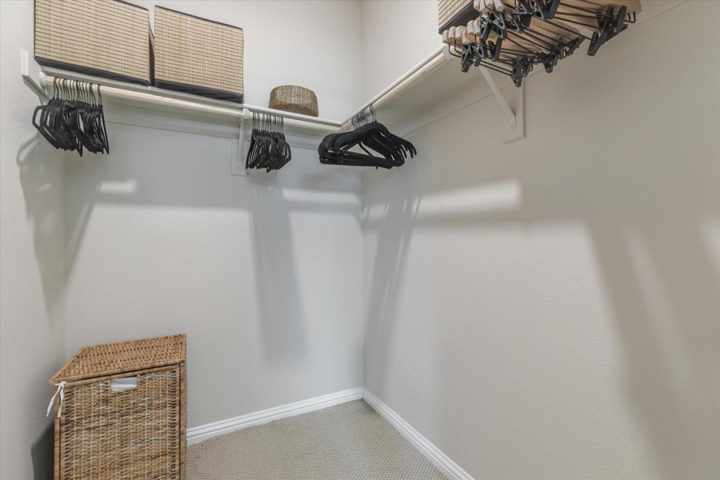 Walk-in closet with corner hanging rods, black hangers, and woven storage baskets.