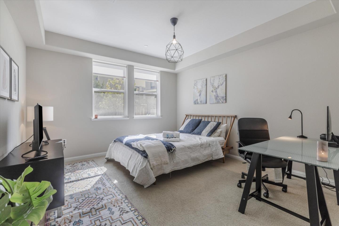 Furnished bedroom with a white-and-blue bed, two windows, and a glass-top desk.