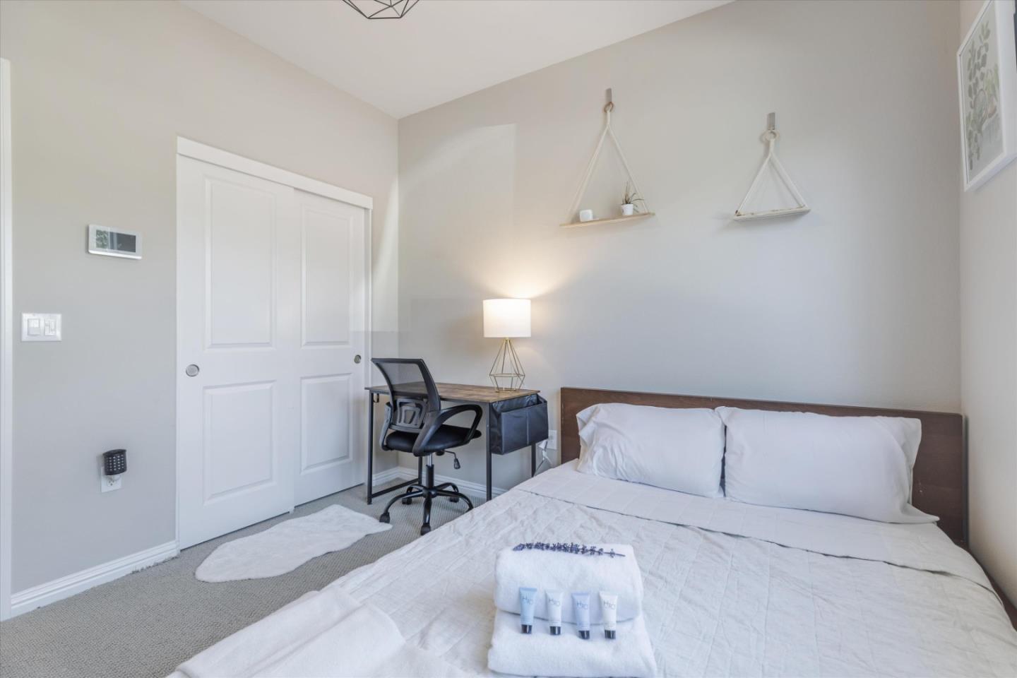 Staged bedroom with a white bed, folded towels, and a desk beside the closet.