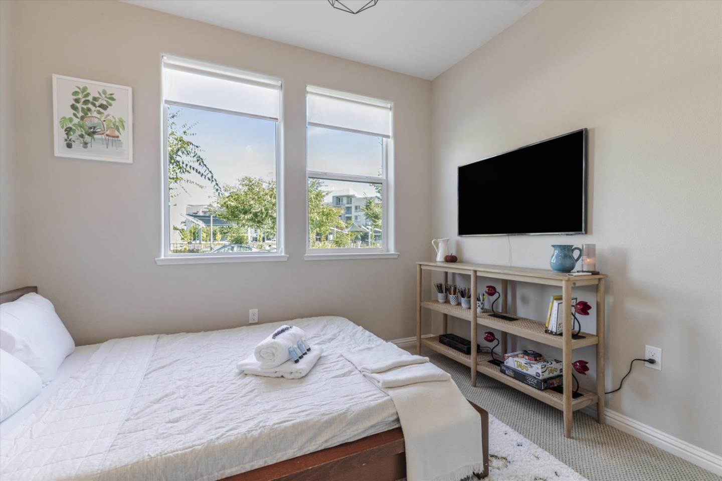 Bedroom with a white bed, two tall windows, and a wall-mounted television above wooden shelving.