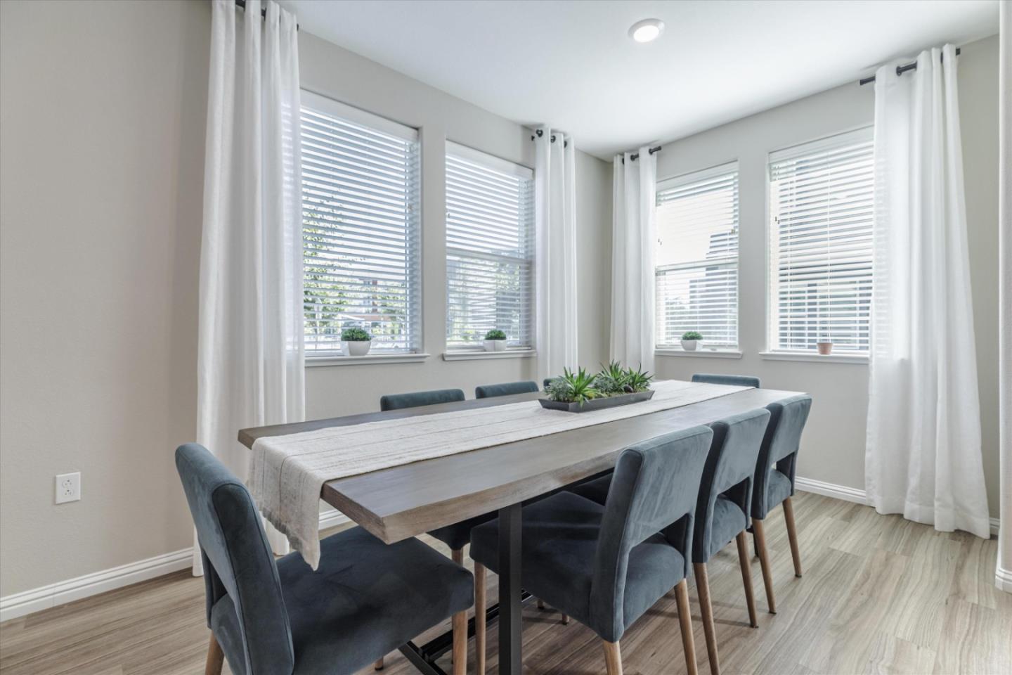 Dining room with a long wood table, blue upholstered chairs, and multiple curtained windows.