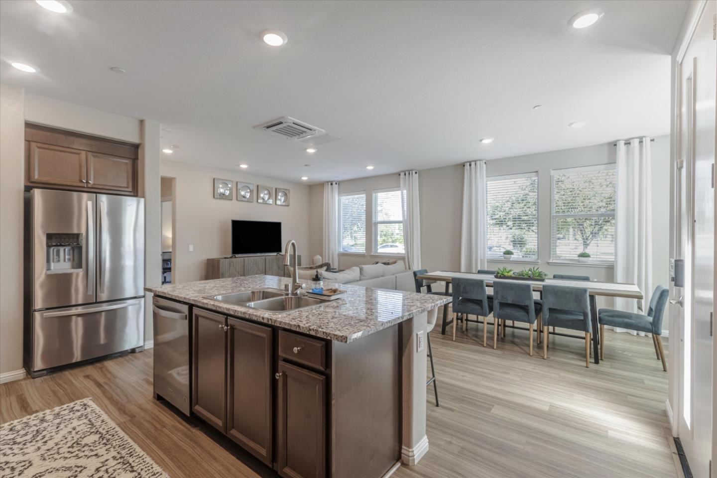Open-plan kitchen with a granite island, stainless steel refrigerator, and adjoining dining area.