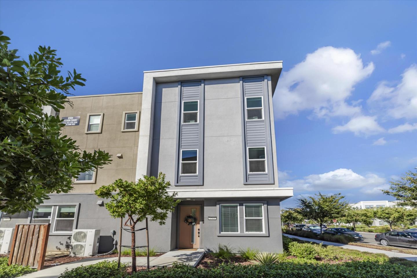 Modern multi-story townhouse with tall narrow windows, a recessed entry, and landscaped front beds.