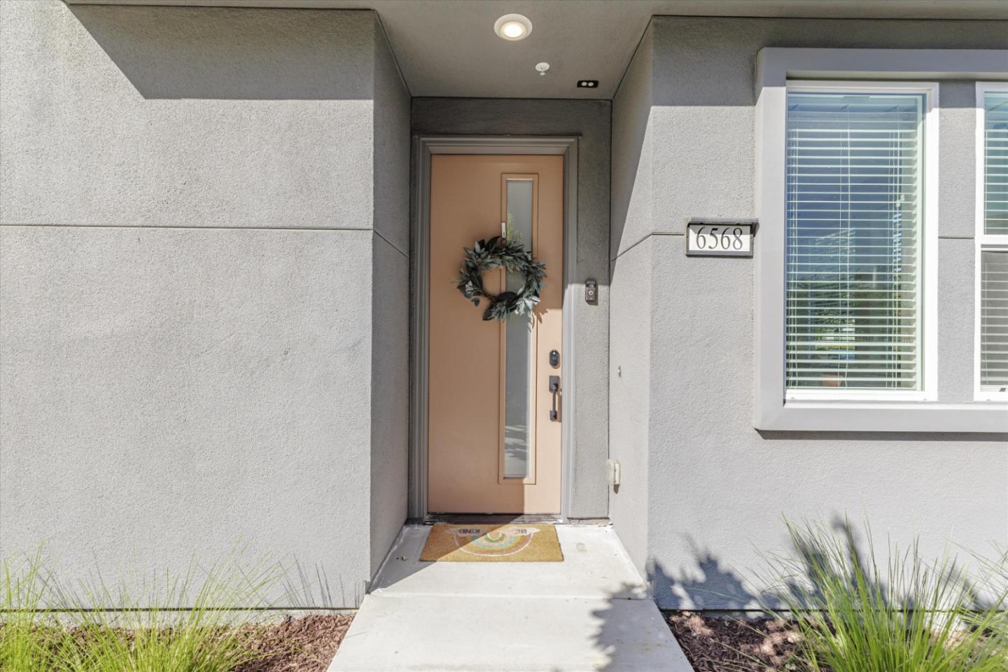 Recessed home entrance with a tan door, wreath, and address plaque reading 6568.