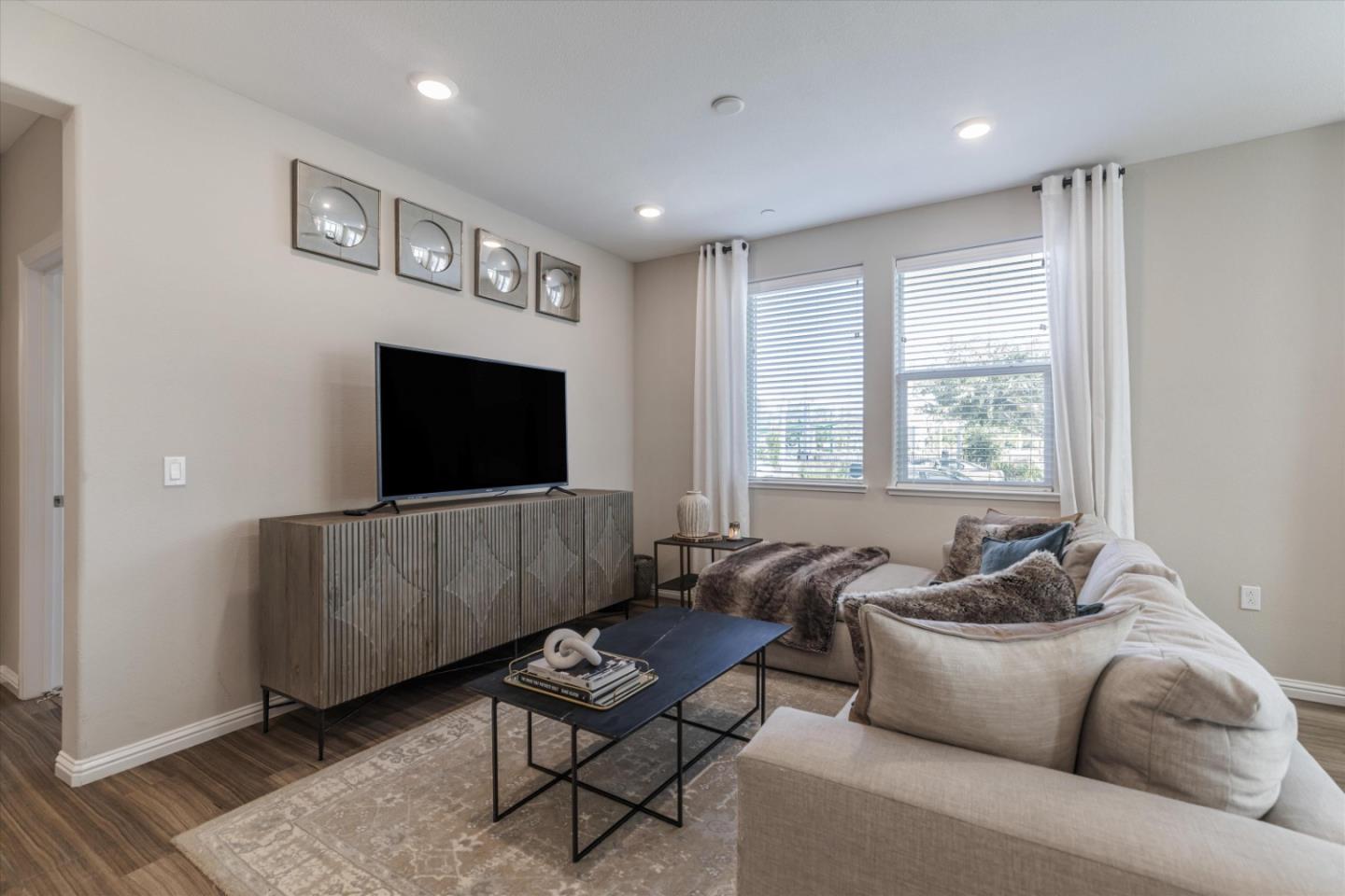 Living room with a light sectional, patterned rug, black coffee table, and television on a wood console.