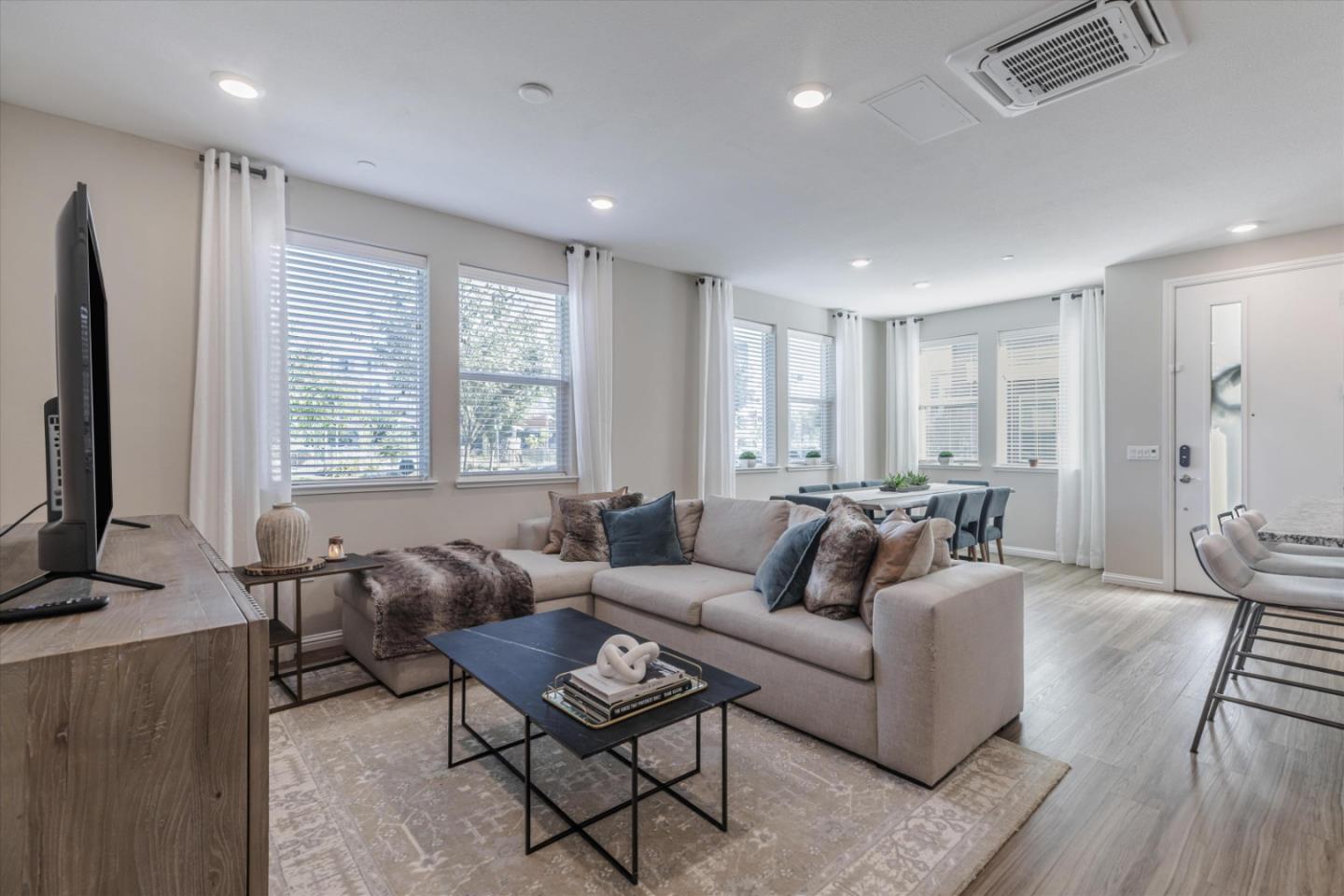 Open-plan living room with a sectional sofa, large curtained windows, and adjoining dining area.