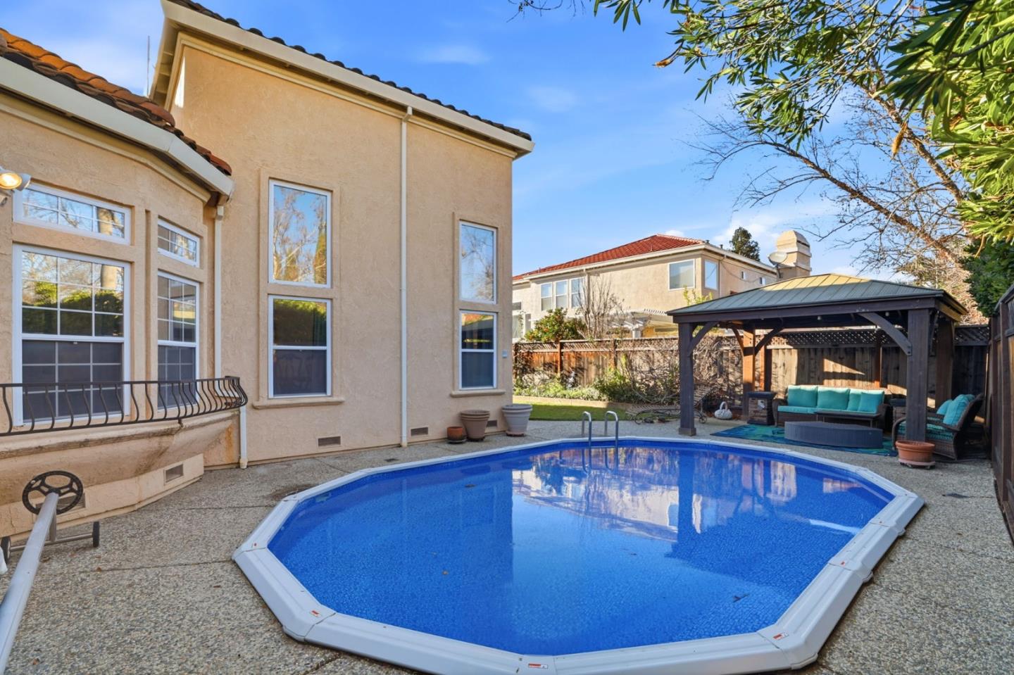 Backyard pool beside a two-story stucco home, with a covered patio and turquoise outdoor seating.