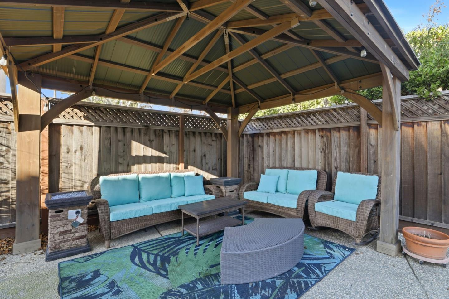 Covered patio with turquoise-cushioned wicker seating beneath a wooden gazebo.