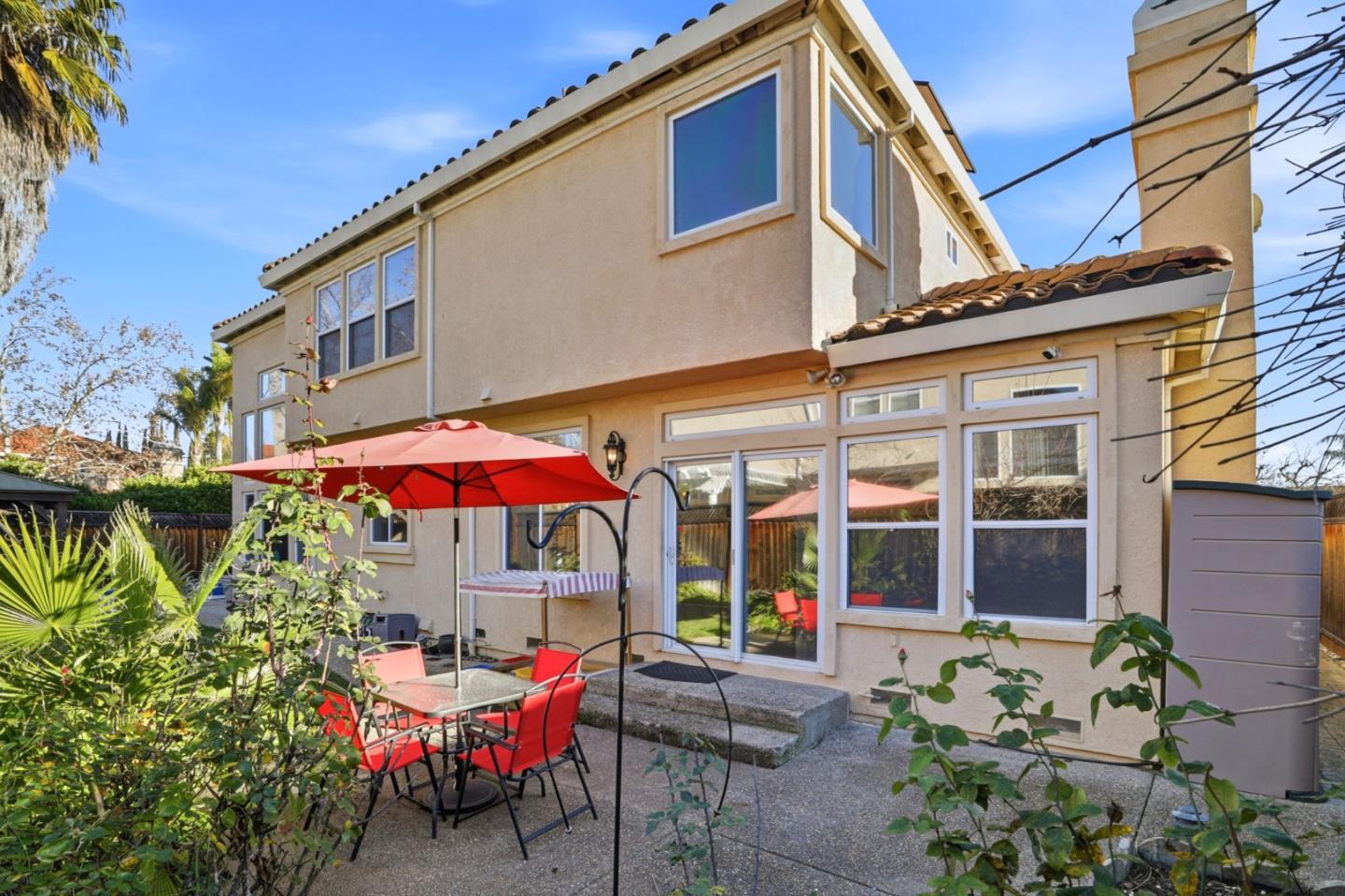 Two-story home’s rear patio with large windows, red umbrella, and outdoor dining set.