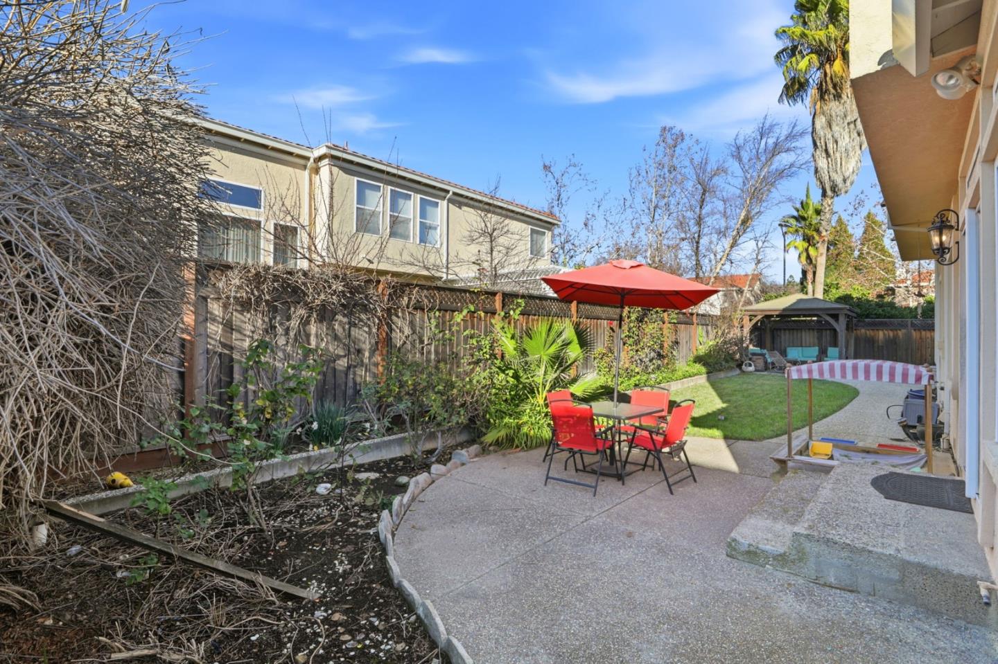 Backyard patio with red umbrella, outdoor dining set, lawn, and covered seating area.