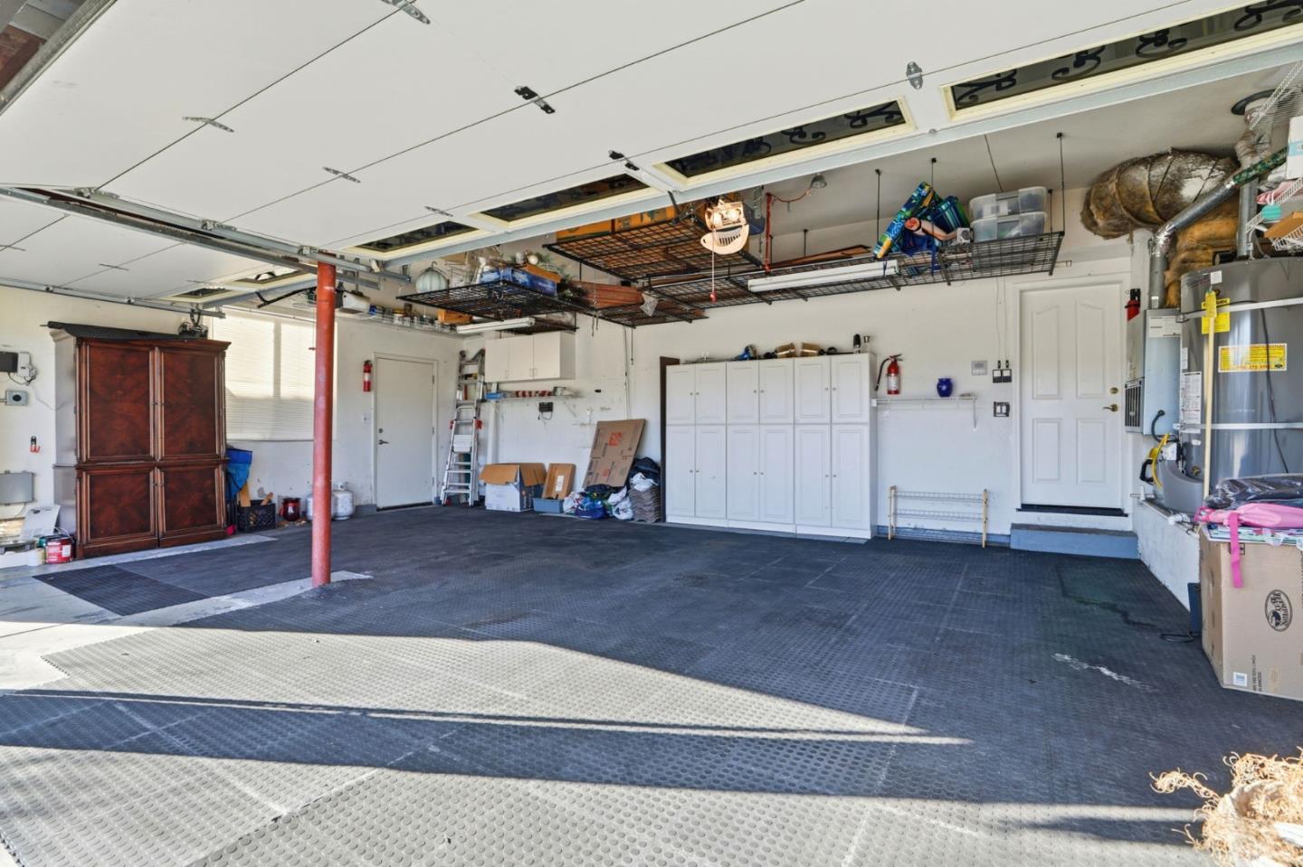 Spacious garage with an open overhead door, dark floor mats, white cabinets, and ceiling storage racks.