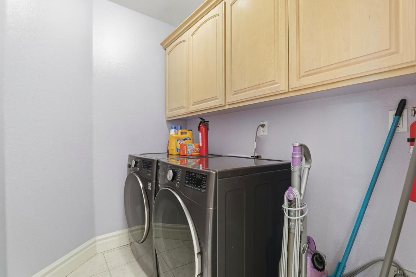 Laundry room with front-loading washer and dryer beneath light wood cabinets.