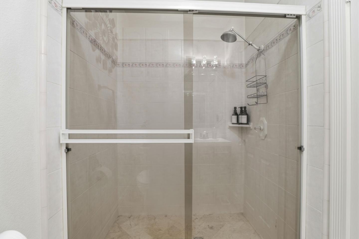 Walk-in shower with a glass enclosure, rain showerhead, decorative tile borders, and stone-look floor.