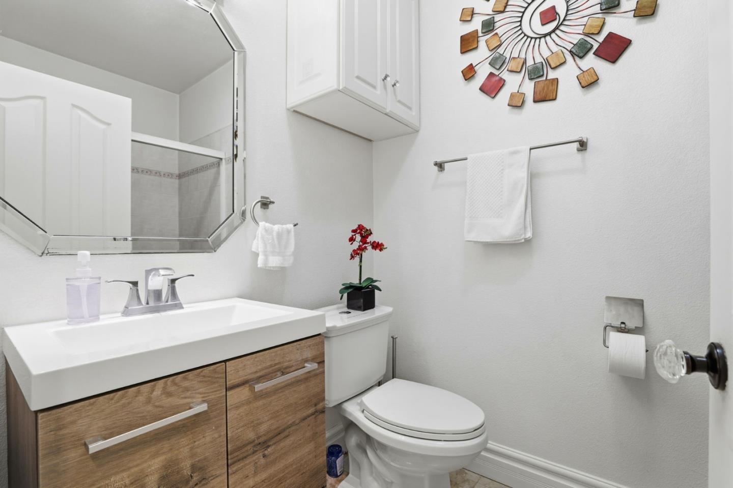 Bathroom with a wood-grain vanity, glass-enclosed shower, and colorful sunburst wall decor.