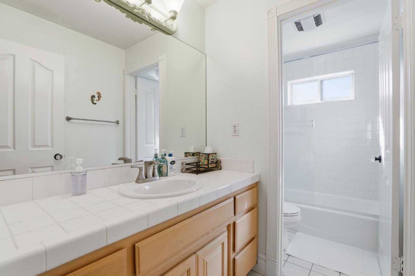 Bathroom with a tiled vanity and wood cabinets beside a white-tiled tub and shower.