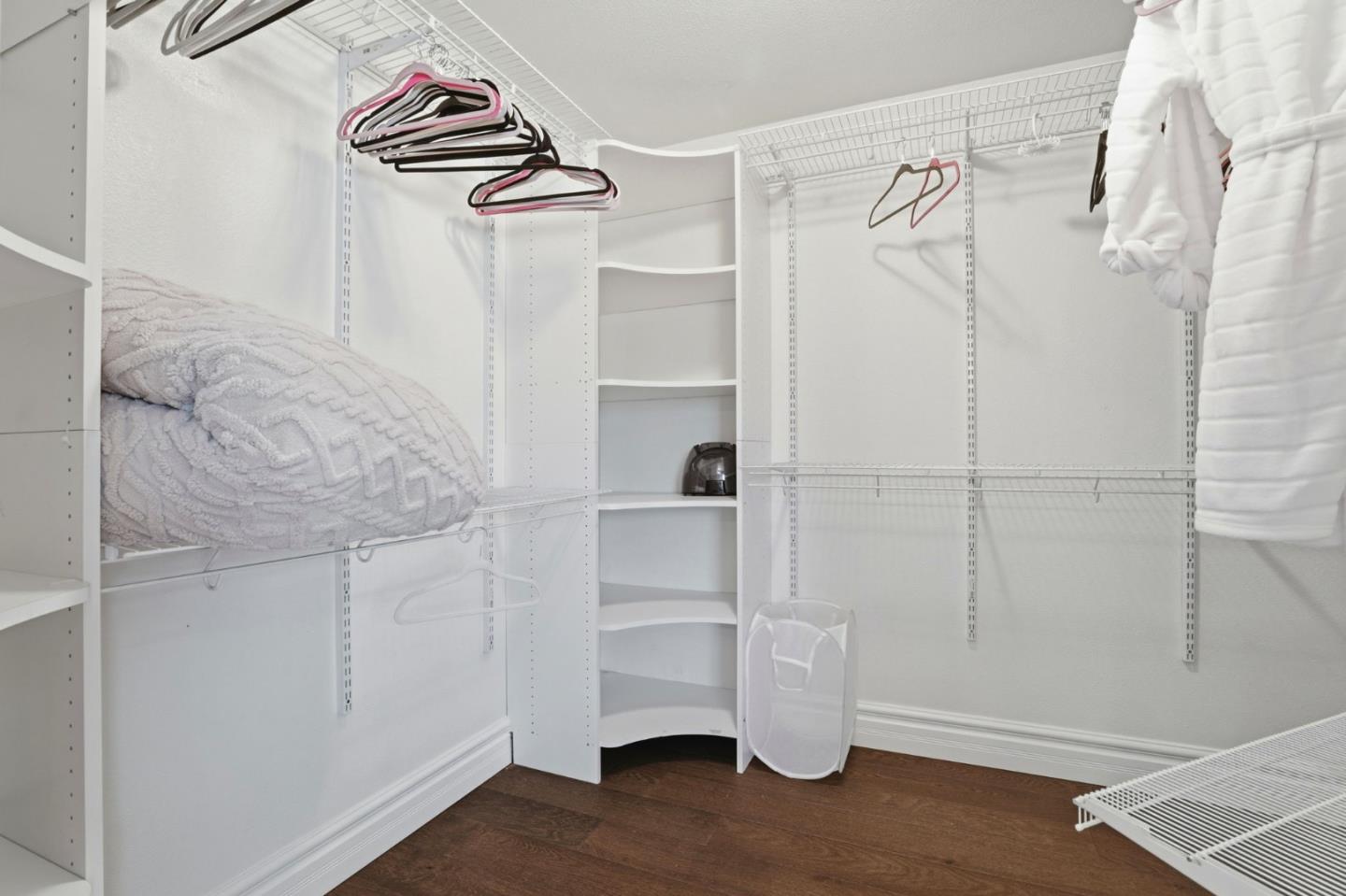 Walk-in closet with white shelving, wire racks, hanging robes, and dark wood flooring.