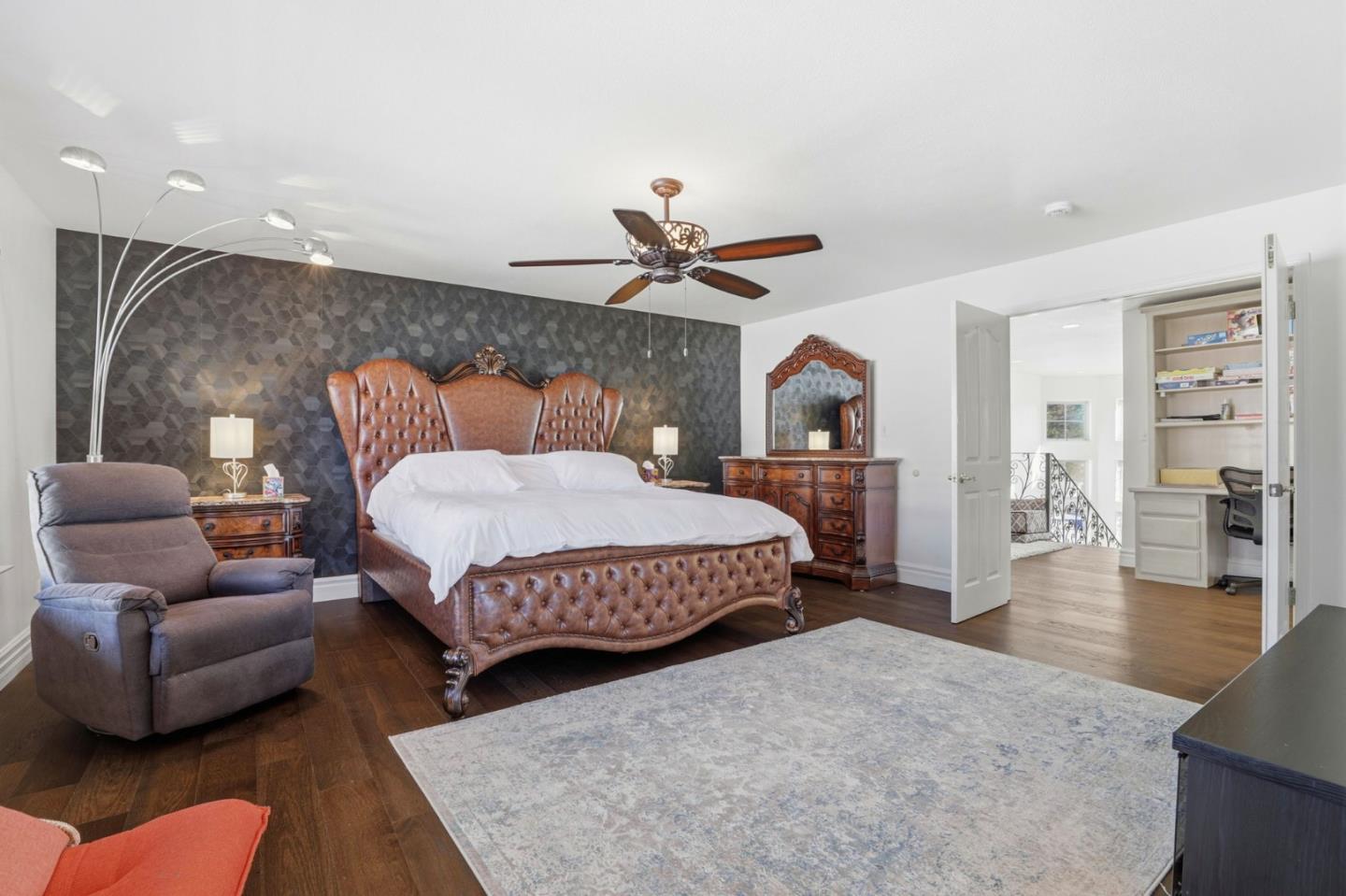 Furnished bedroom with a tufted leather bed, dark geometric accent wall, and wooden dressers.