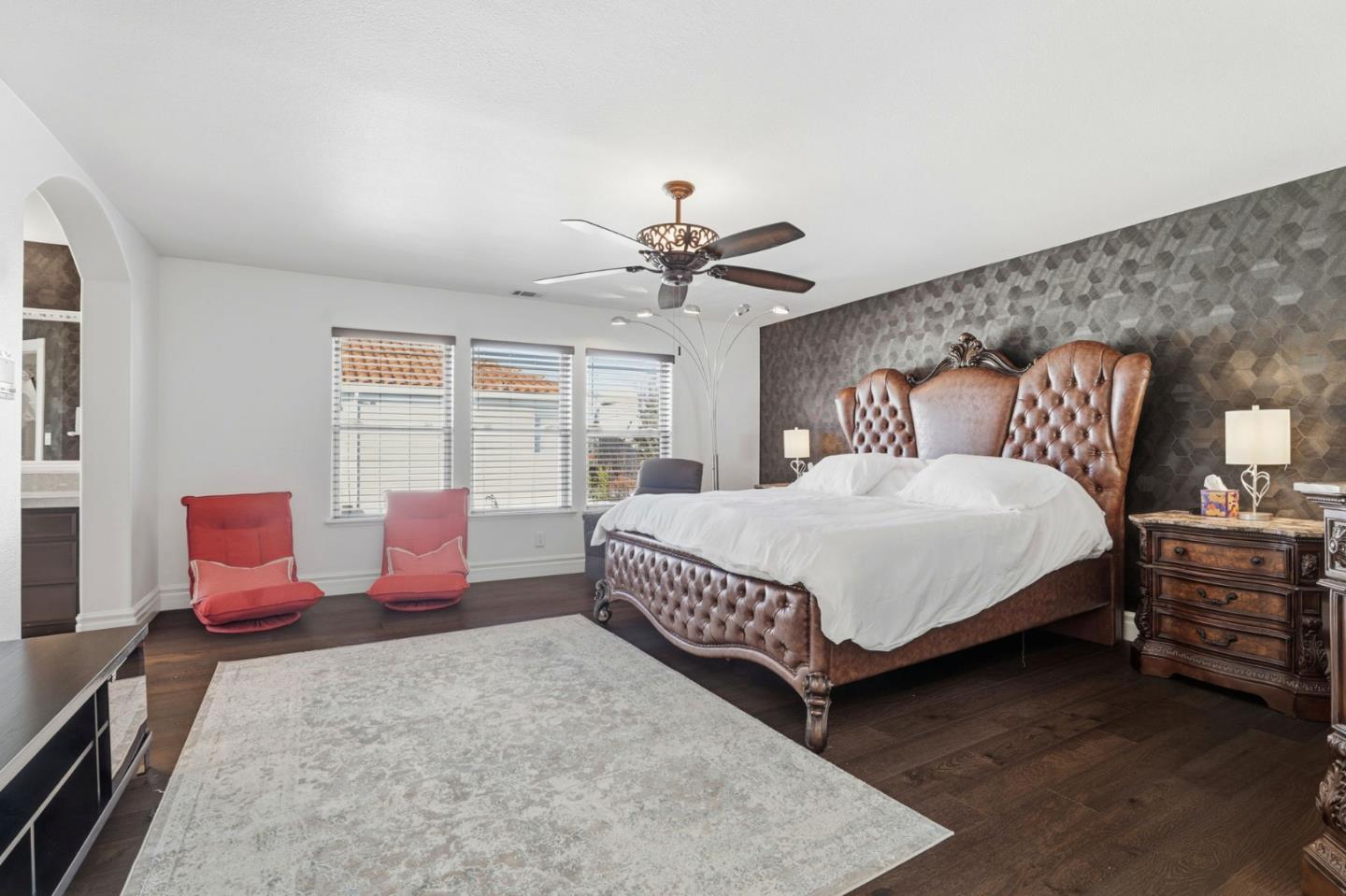 Bedroom with a tufted leather bed, patterned accent wall, and two red chairs.