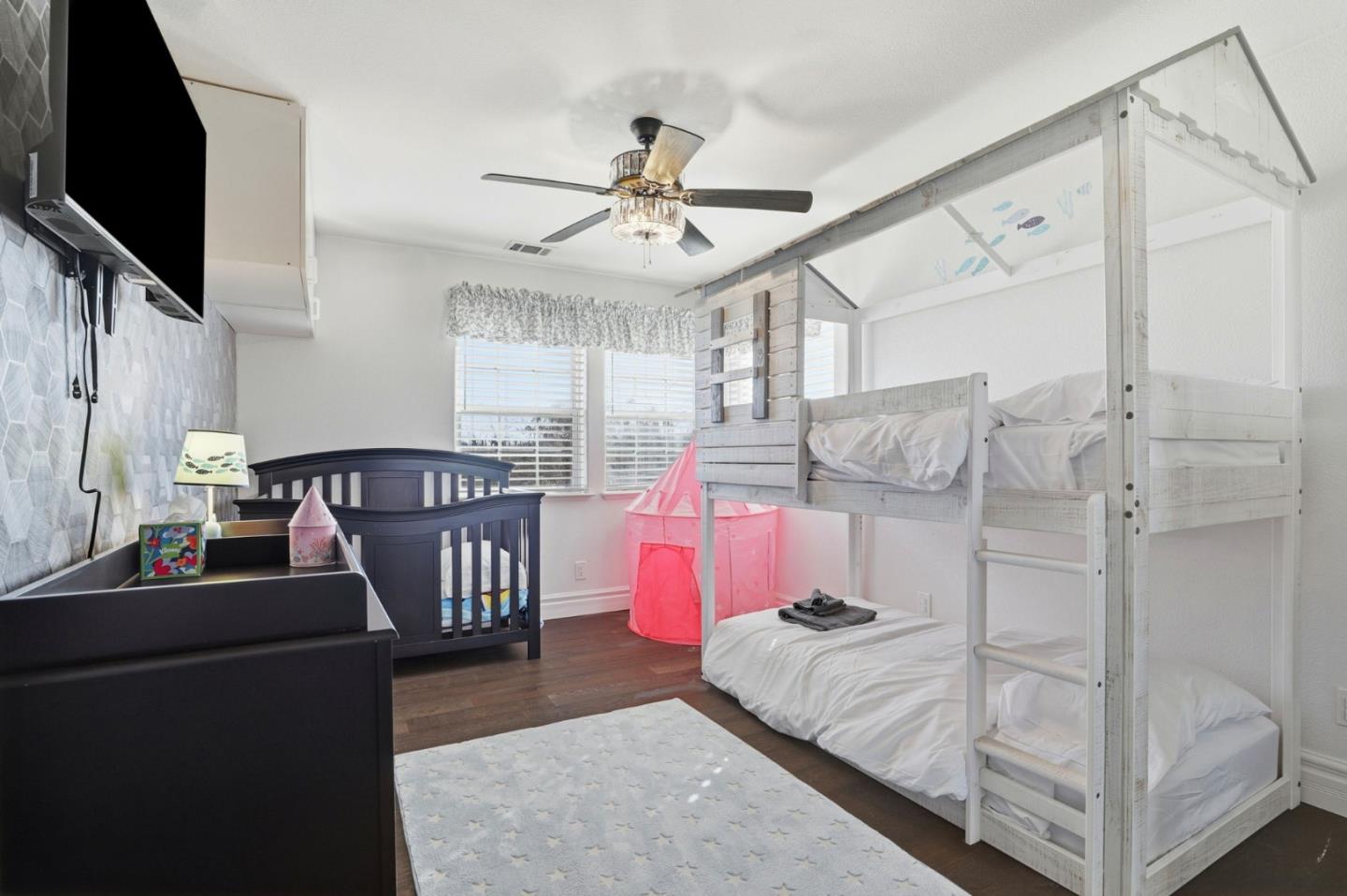 Bedroom with a white bunk bed, dark crib, and pink play tent.