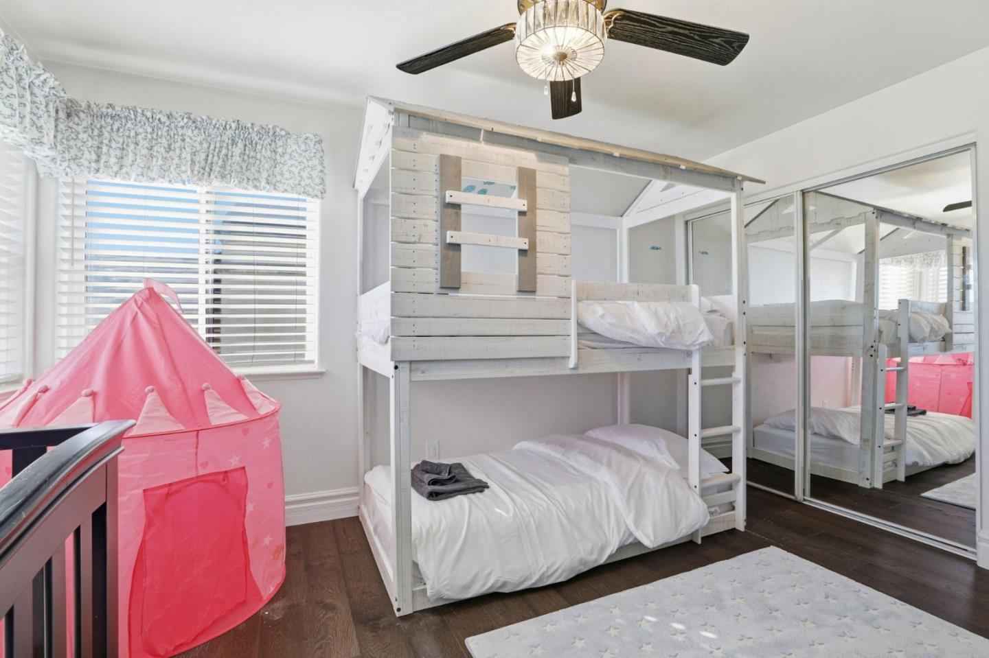 Children’s bedroom with a white bunk bed, mirrored closet doors, and a pink play tent.